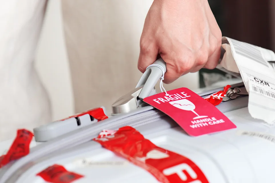 Nha Trang: Man holding white suitcase in hand at airport of Cam Ranh. Bright red luggage tag (Fragile, Handle with care) attached to plastic suitcase.