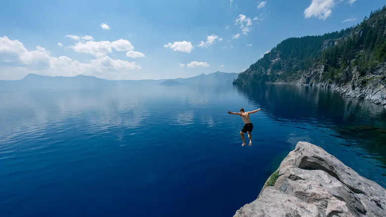 A man jumps into the waters of Crater Lake from a rock outcrop