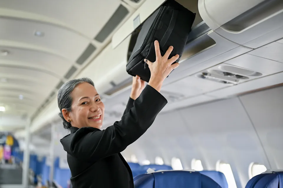 An attractive senior female passenger is putting her luggage in an overhead locker before takeoff. People and transportation concept