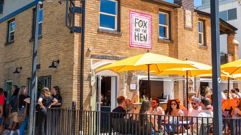 Exterior of Fox and the Hen with people sitting outside on the patio under yellow umbrellas