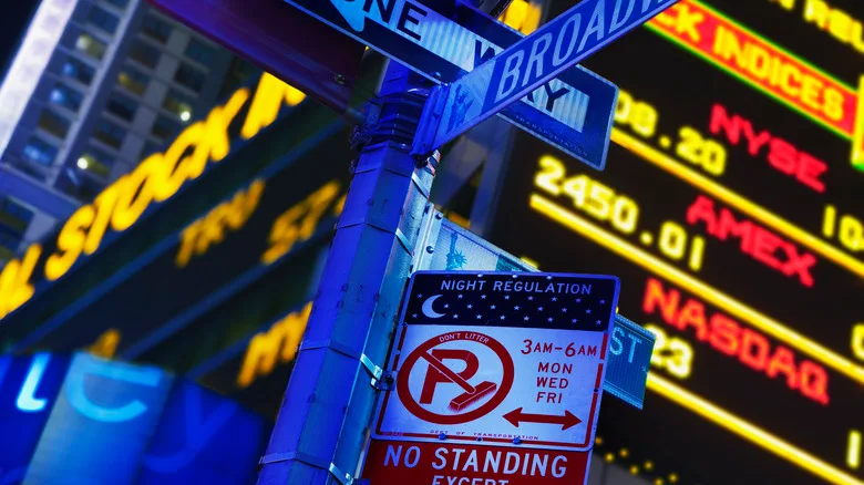 A cluster of confusing street signs hang in front of the stock market ticker in New York City