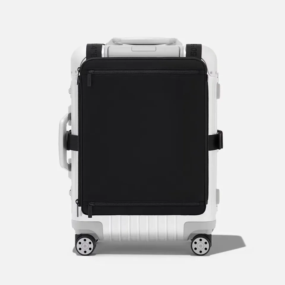 White hard-shell suitcase with black zippered front pocket and four wheels on a white background.