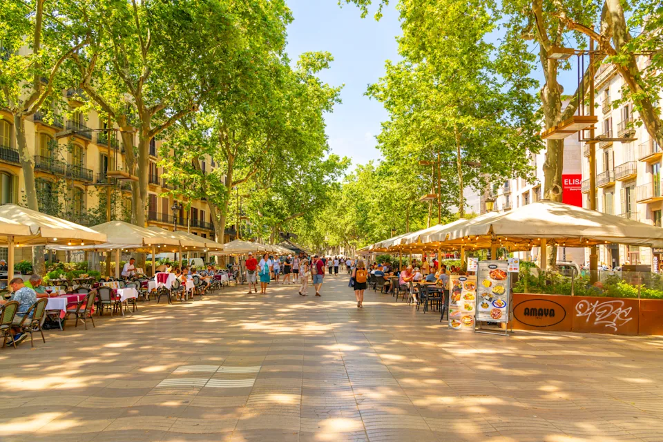 Bustling pedestrian street in a European city lined with outdoor cafes, trees, and people strolling and dining