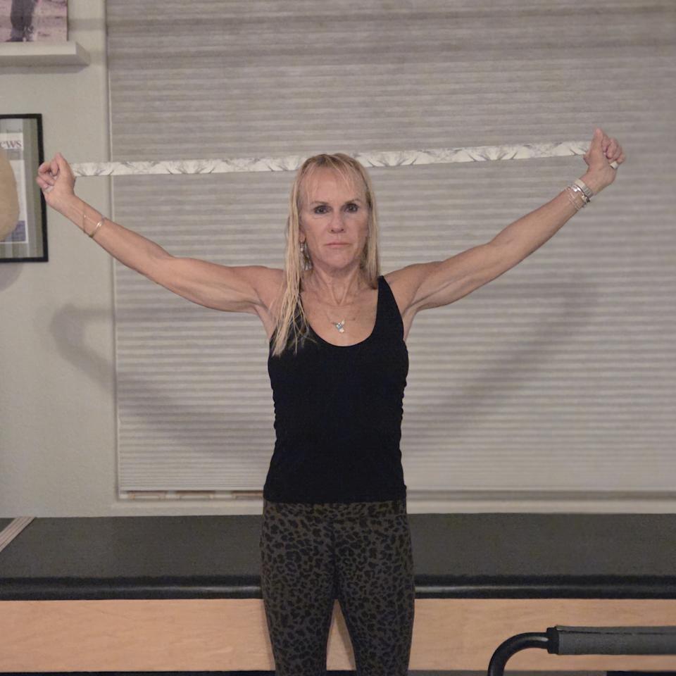 Woman stretching with yoga strap in front of a Pilates reformer bed